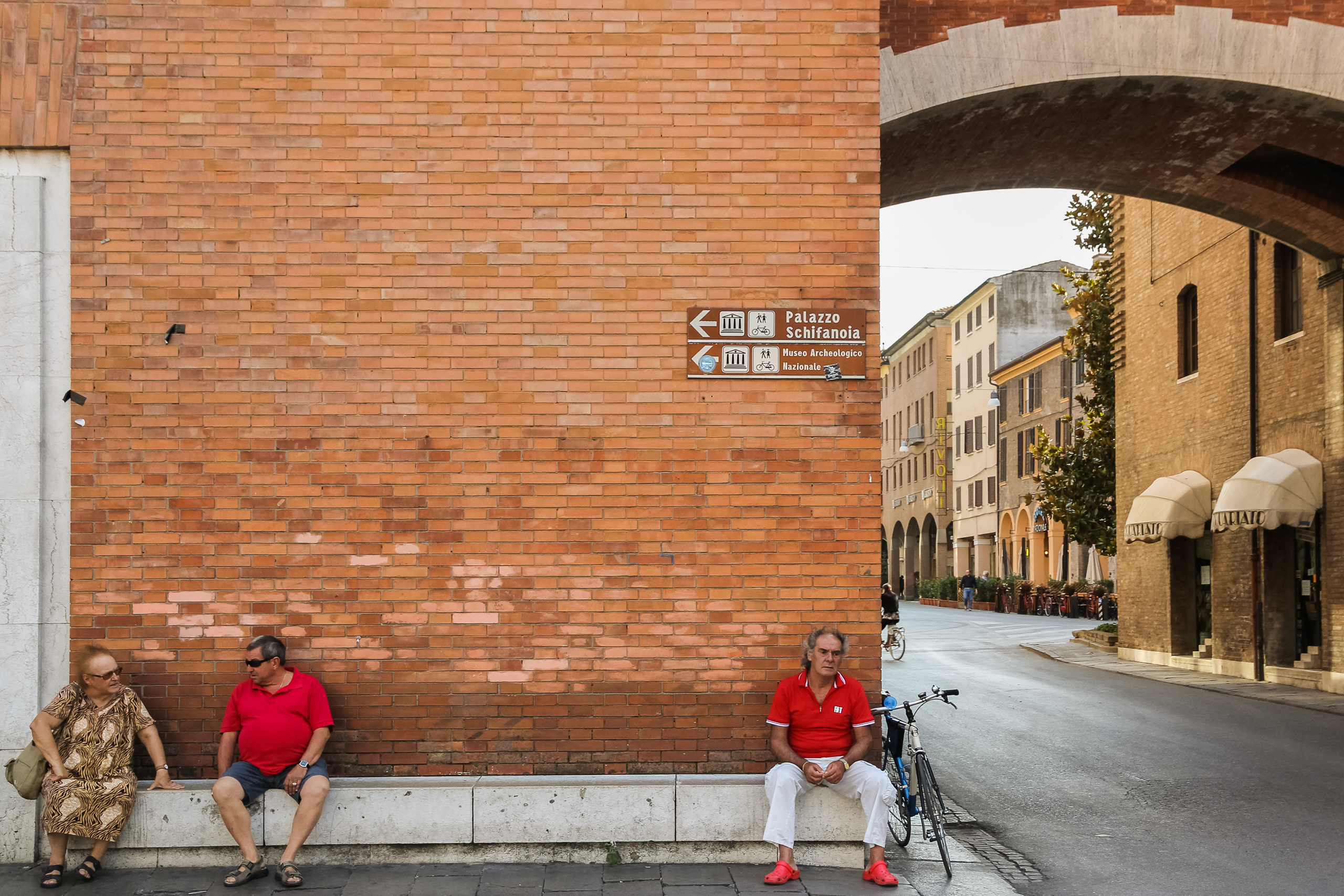 Sitzen an der Ziegelwand, der Wegweiser zeigt zum Palazzo Schifanoia